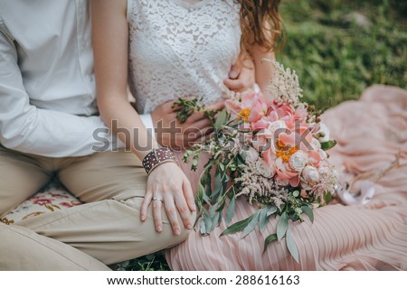 couple sitting on the grass and holding a bouquet of pink and white peonies and green