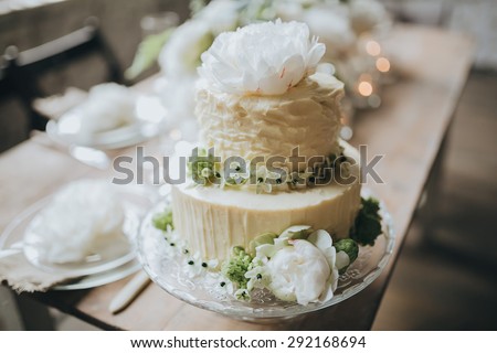 white cake decorated with flowers, berries and greens costs on a wooden table decorated loft with white brick walls and wooden floor