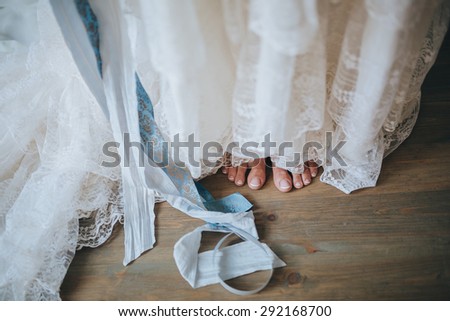 girl in a white wedding dress with blue ribbon standing barefoot on a vintage wooden floor boards of the