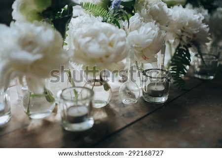 white peonies are in glass bottles next to the candles on vintage wooden table in the loft
