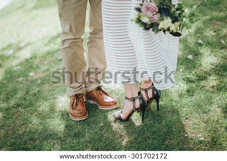man in beige trousers and brown leather shoes and a girl in a white dress and shoes with a bouquet standing on the green grass