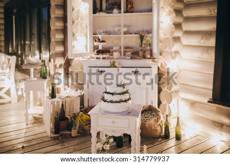 a white wedding cake decorated with greenery is on the stand in candy-bar