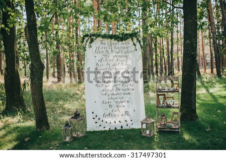 a place for a wedding ceremony on a green lawn in the forest, decorated with cloth with the inscription and decorative elements