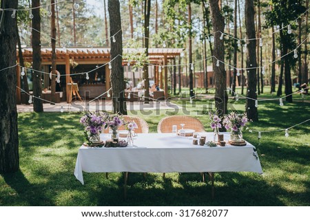 decorated table for the bride and groom standing on a green lawn in a pine forest