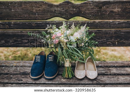 bouquet of flowers and greenery and shoes bride and groom lying on an old wooden bench