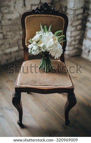 bridal bouquet of white flowers and greenery is on a vintage chair against a white brick wall in loft
