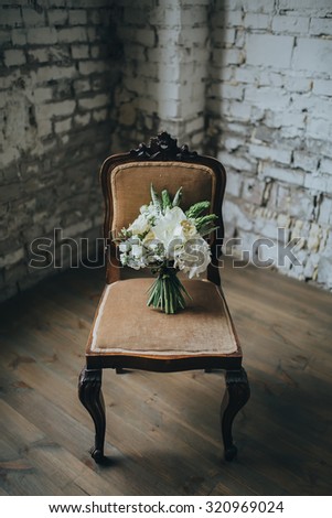 bridal bouquet of white flowers and greenery is on a vintage chair against a white brick wall in loft