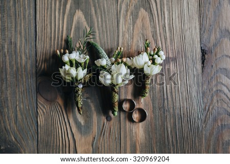 wedding rings bride and groom lying on a vintage wooden floor near the boutonniere of flowers and greenery
