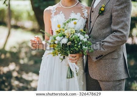 bride and groom standing on green grass and holding a bouquet of white and yellow flowers with green