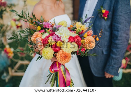 bride in a white dress and groom in a suit holding a bouquet of red flowers, orange flowers and greenery