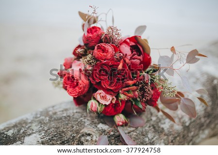 Wedding bouquet . The bride\'s bouquet. Bouquet of red and pink flowers, black berries and greenery, with a ribbon of color Marsala lies on a log by the lake