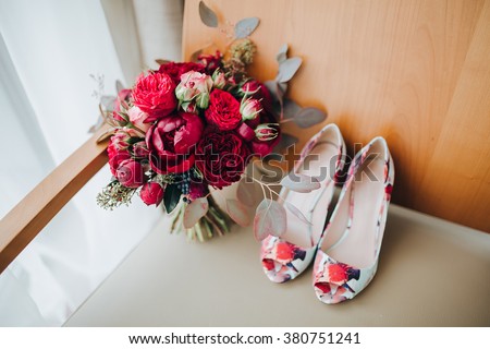 Wedding. The bride\'s bouquet. Wedding bouquet . A bouquet of red flowers, black berries and greens lying on a chair near the window next to the bride\'s shoes
