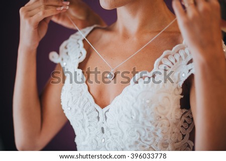 Wedding. Jewelry. The bride in a white dress putting on a necklace around his neck