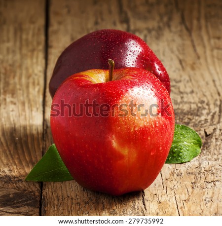 Two red apples with water drops on a wooden table, selective focus