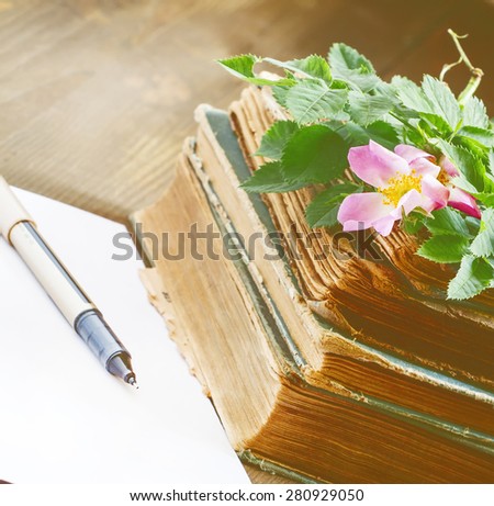 Old books, blank paper, flowers of wild roses in vintage style, selective focus