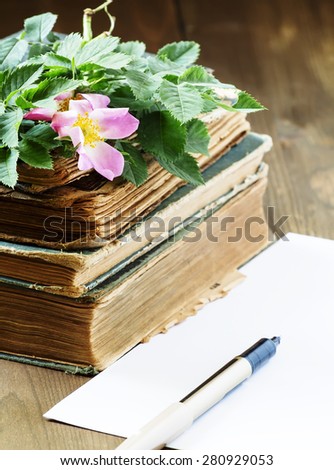 Old books, blank paper, flowers of wild roses in vintage style, selective focus