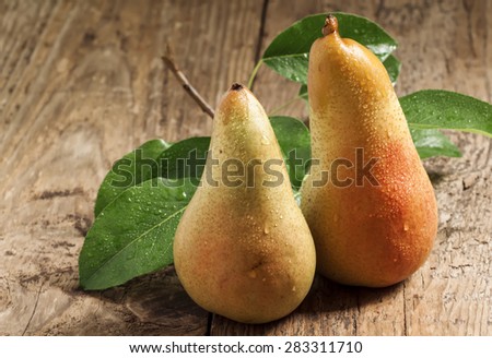 Two ruddy long yellow pears with leaves on the old wooden table, selective focus