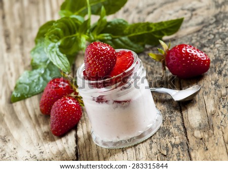 Homemade strawberry yogurt with fresh strawberries and mint in a jar on a wooden background, selective focus