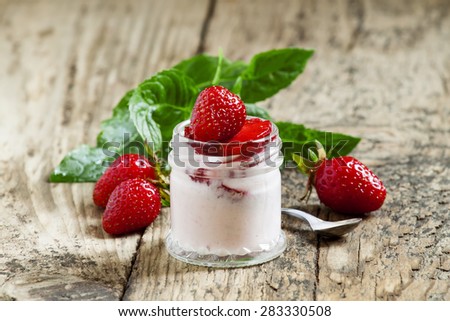 Homemade strawberry yogurt with fresh strawberries and mint in a jar on a wooden background, selective focus