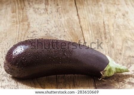 Big aubergine with drops of water on wooden table, selective focus