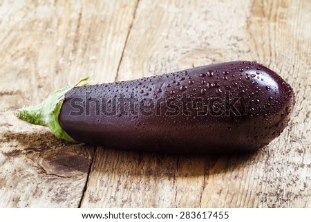 Big aubergine with drops of water on wooden table, selective focus