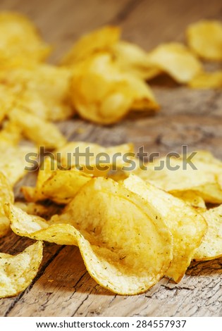 Golden potato chips on an old wooden table, unhealthy eating concept, selective focus