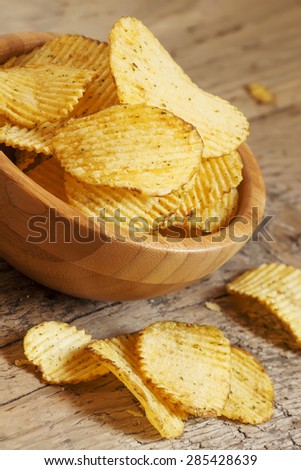 Rippled potato chips in a wooden bowl on the old table, selective focus