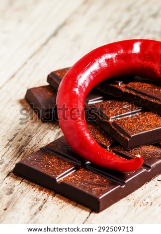 Chopped dark chocolate, red hot chili pepper and ground red pepper on an old wooden table, selective focus