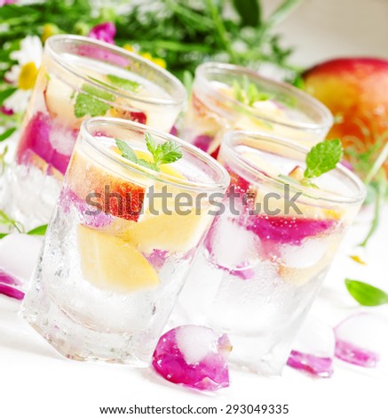 Fresh sparkling beverage with peaches and ice with rose petals on white wooden background, selective focus
