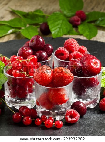 Assorted summer berries: raspberries, red currant, cherry, strawberry with glasses on black background, selective focus