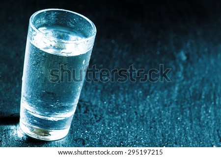 Glass with a transparent drink on dark background, black and white, selective focus