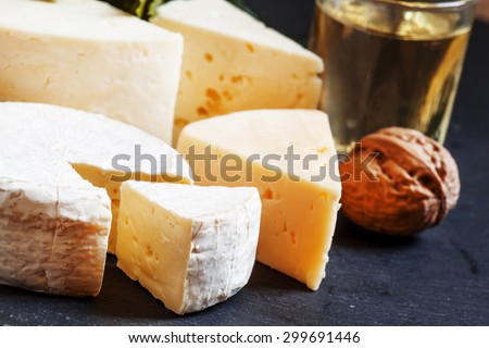 Assorted different kinds of cheese, nuts, herbs, white wine on a dark stone plate, selective focus