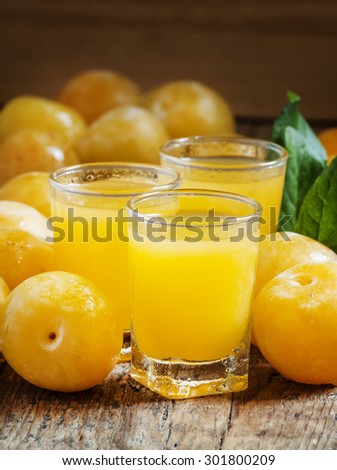 Delicious fresh juice of yellow sweet plums in a glass on the old wooden background, selective focus