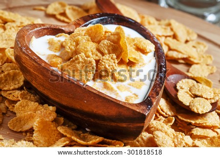 Corn flakes with milk in a wooden bowl in the shape of a heart, selective focus