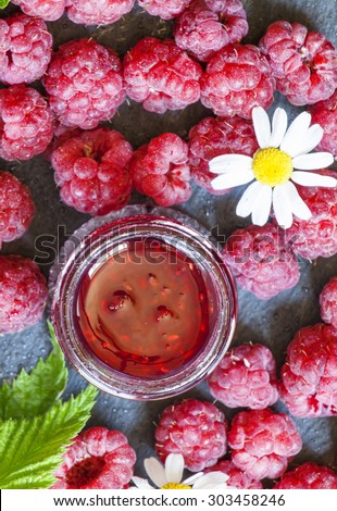 Raspberry jam and fresh raspberries with leaves, flowers, meadow of daisies, top view, selective focus