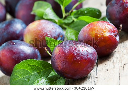 Delicious blue-orange plums with drops of water on the old wooden background, selective focus