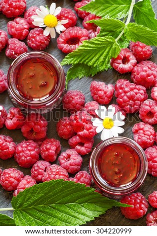 Raspberry jam and fresh raspberries with leaves, flowers, meadow of daisies, top view, selective focus