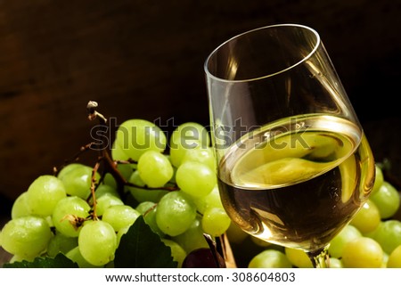 White wine in a glass and green and red grapes in a wicker basket, still life in a rustic style, toned image, selective focus