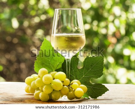 Coid white wine and green grapes on natural blurred background with bokeh, selective focus