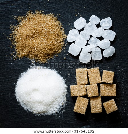 Assortment of sugar: white sand, candy sugar, brown sugar into pieces and brown sugar on a dark background, top view