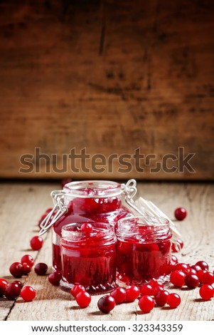 Delicious cranberry jam in glass jars and fresh cranberry on an old wooden background in rustic style, selective focus