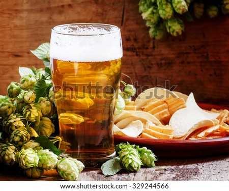 Beer in a glass, chips on the plate, bunch of fresh hops, on the old wooden background, selective focus