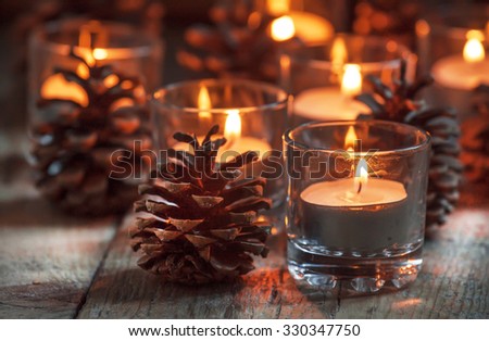 Christmas Christmas card with glowing small candle and fir cones on old wooden background, dark toned image in country style, selective focus