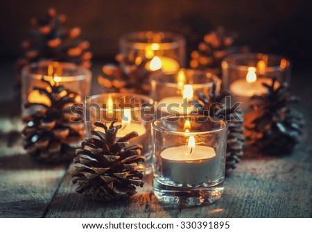 Christmas Christmas card with glowing small candle and fir cones on old wooden background, dark toned image in country style, selective focus