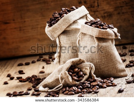 Grains of roasted coffee in bags on old wooden table in rustic style, selective focus