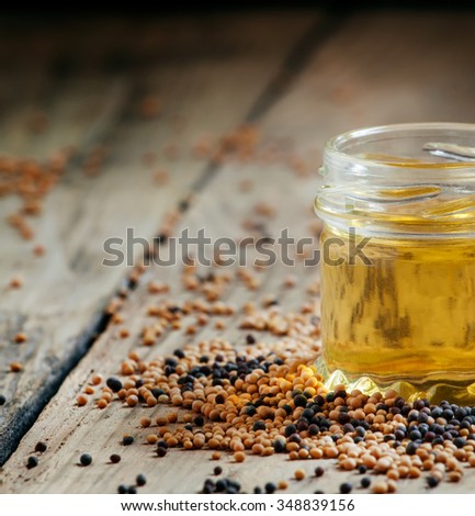 Oil of mustard in a small jar and yellow and black mustard seeds on an old wooden table in rustic style, selective focus