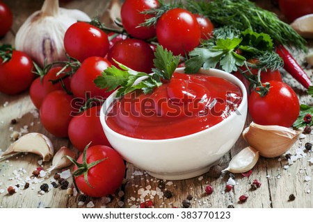 Tomato ketchup sauce with garlic, spices and herbs with cherry tomatoes in a white porcelain bowl on old wooden table, selective focus