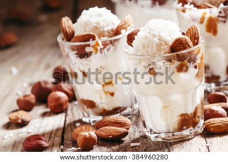 Dessert with vanilla ice cream, nut sauce, almonds, hazelnuts and coconut, served in glasses, selective focus