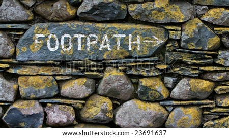 Footpath sign on stone wall with yellow lichen