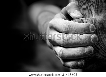 Chalked hand grips tightly to hang off an artificial climbing hold. Converted to black and white; shallow depth of field